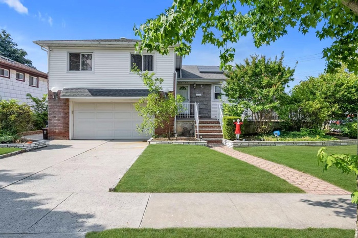 Tri-level home with roof mounted solar panels, roof with shingles, a front lawn, and concrete driveway