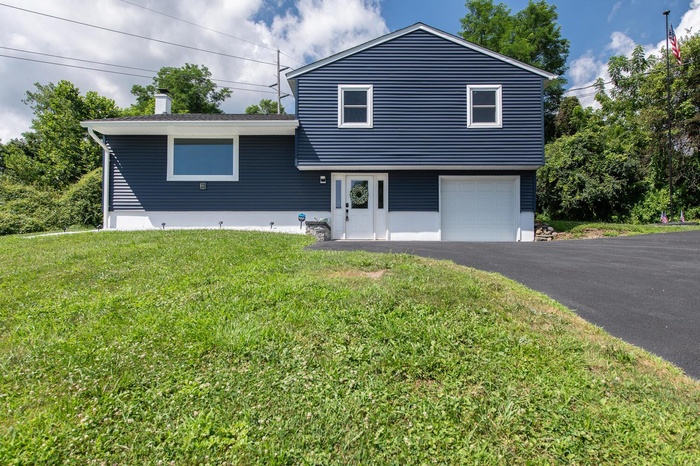 Split level home featuring an attached garage, a chimney, driveway, and a front lawn