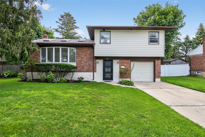 Tri-level home with brick siding, an attached garage, driveway, and a chimney