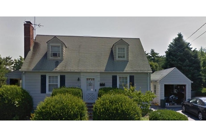 Cape cod house with an attached garage, a chimney, and an outbuilding