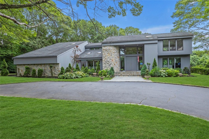 Contemporary inspired home featuring stone and cedar siding, front lawn, circular driveway and a 3-car garage.
