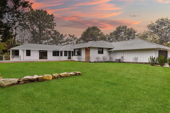 Back of house at dusk featuring a lawn, a shingled roof, an attached garage, cooling unit, and brick siding