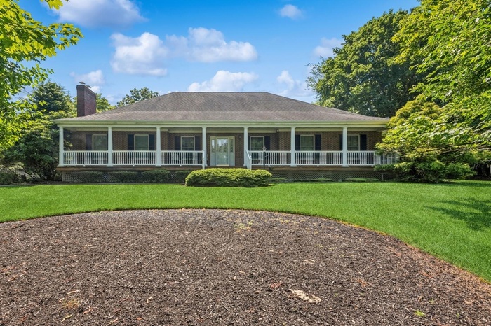 Country-style home featuring a porch, brick siding, a chimney, and a front lawn