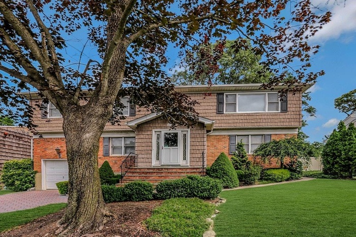 View of front of house with a front lawn, a garage, driveway, and brick siding