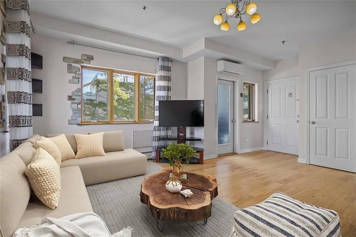 Living room with baseboards, baseboard heating, light wood-type flooring, an AC wall unit, and a notable chandelier