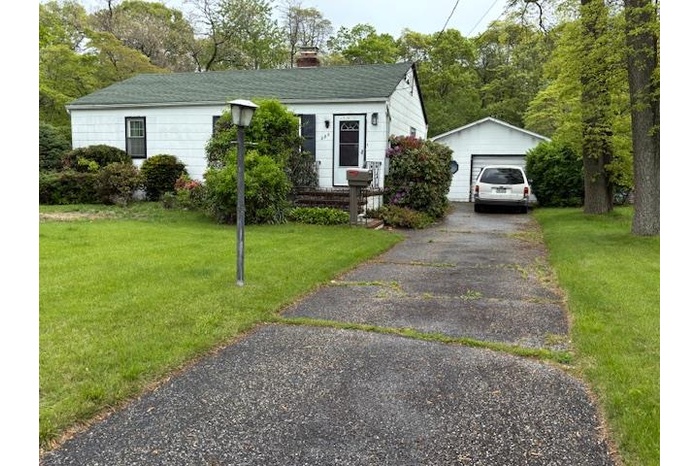 View of front of property featuring an outbuilding, a detached garage, a chimney, and a front yard