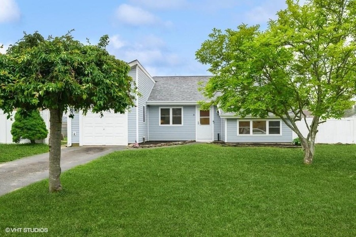 View of property hidden behind natural elements with concrete driveway, roof with shingles, and an attached garage