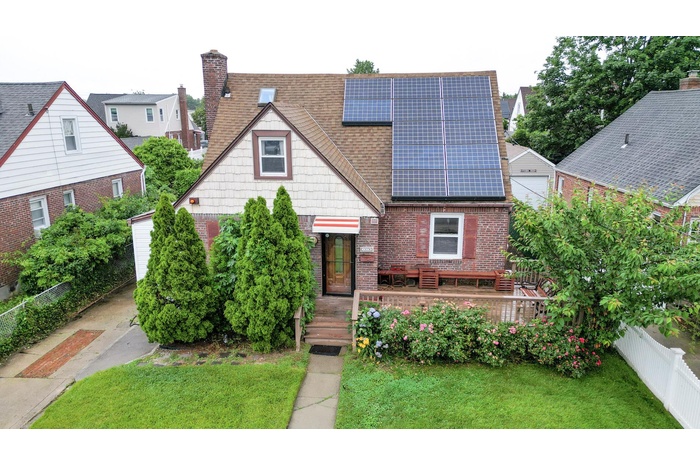 View of front of house featuring a shingled roof, solar panels, brick siding, a fenced backyard, and a chimney