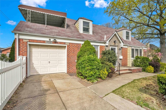 Cape cod house with brick siding, a garage, fence, and driveway