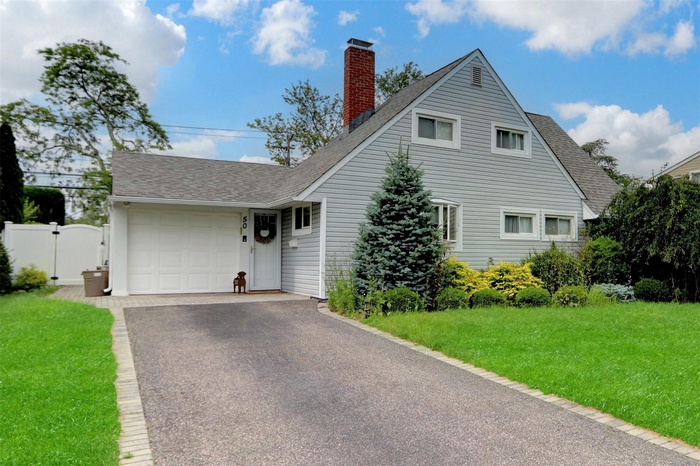 View of front of property featuring a shingled roof, an attached garage, driveway, a chimney, and a front lawn