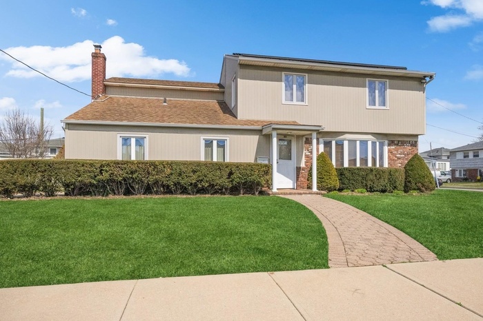 View of front of home featuring a front yard, a chimney, and brick siding