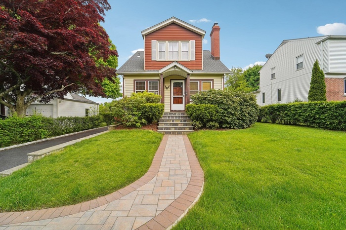 View of front of home featuring a chimney, a front lawn, and roof with shingles