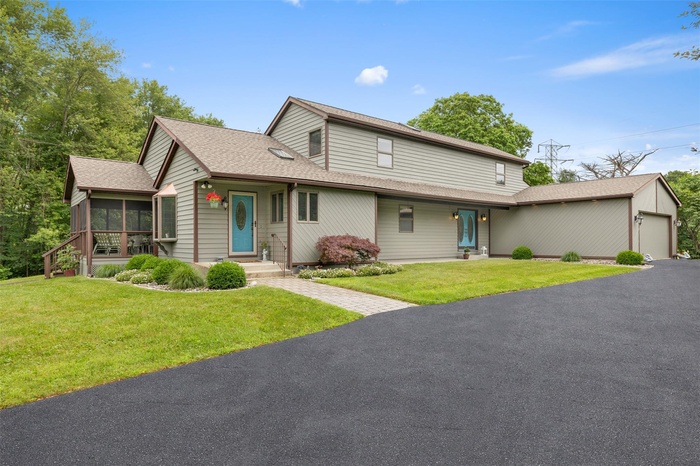 View of front of property featuring a sunroom, an attached garage, a front lawn, and driveway