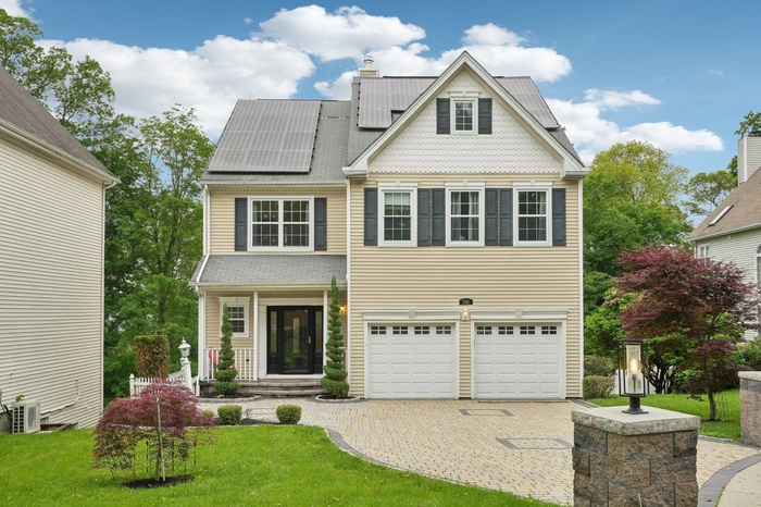 View of front of home with decorative driveway, a garage, solar panels, and a front lawn