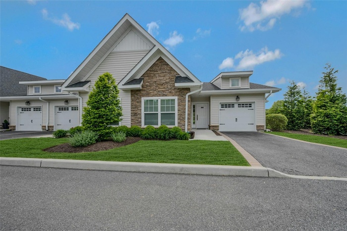 View of front of property with driveway, a front yard, and stone siding