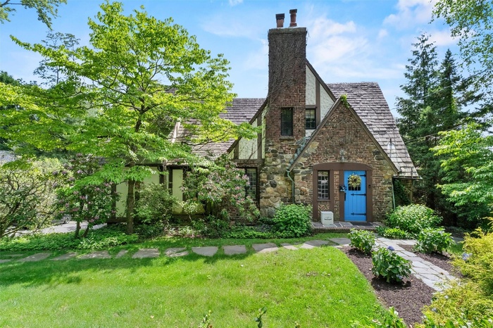 Tudor home featuring stone siding, a front lawn, and a chimney