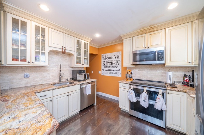 Kitchen with appliances with stainless steel finishes, a sink, cream cabinets, decorative backsplash, and baseboards