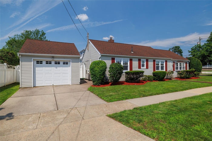 View of front facade featuring an outdoor structure, driveway, a detached garage, roof with shingles, and a chimney