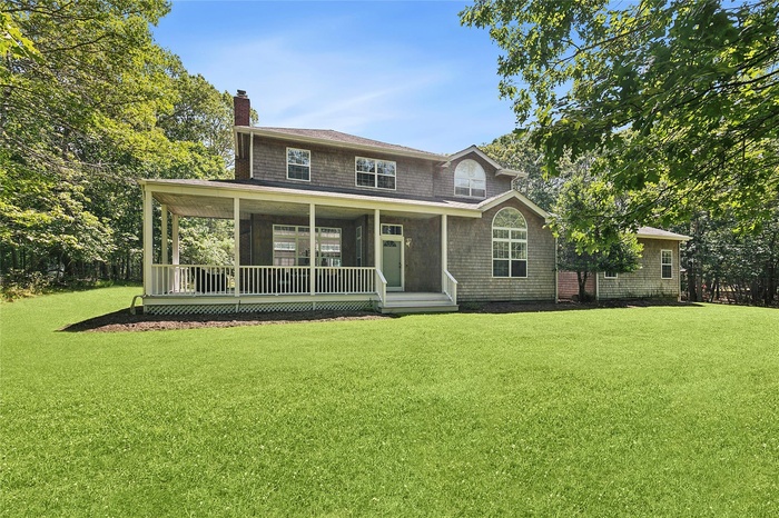 View of front facade featuring a front yard, a chimney, and a porch