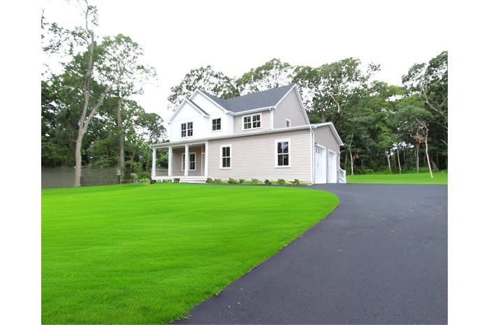View of front of house with a porch, a front yard, driveway, view of scattered trees, and a garage