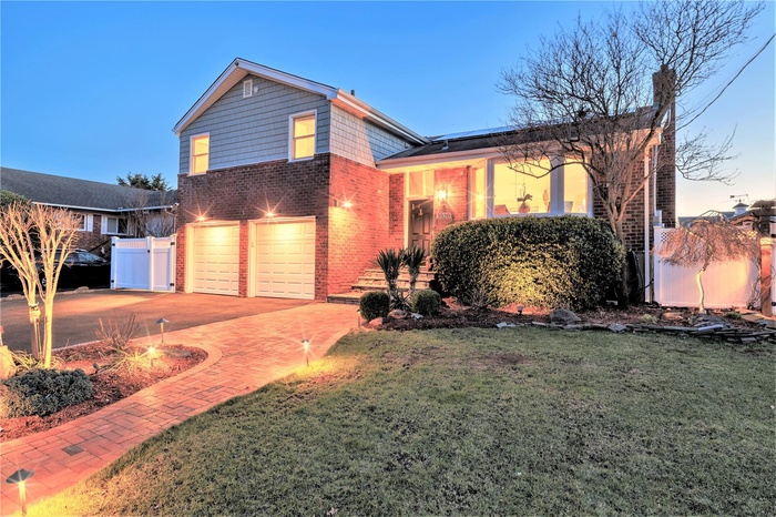 View of front of home with decorative driveway, roof mounted solar panels, brick siding, an attached garage, and a gate