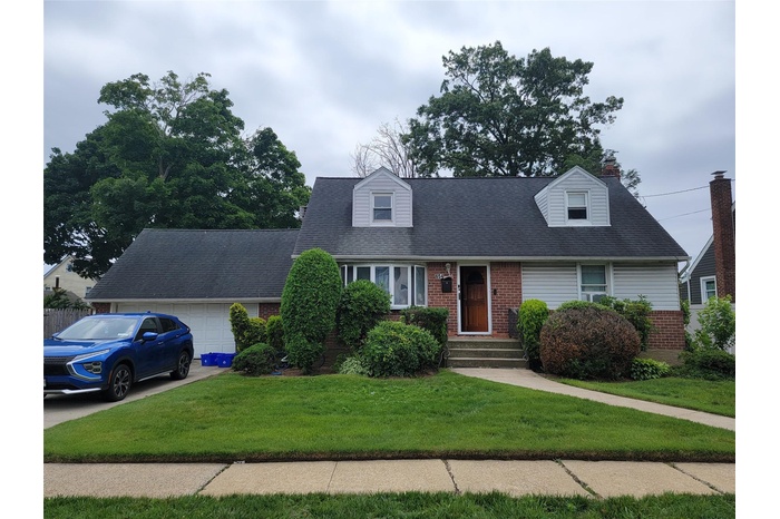 Cape cod-style house featuring brick siding, an attached garage, a front lawn, a chimney, and concrete driveway