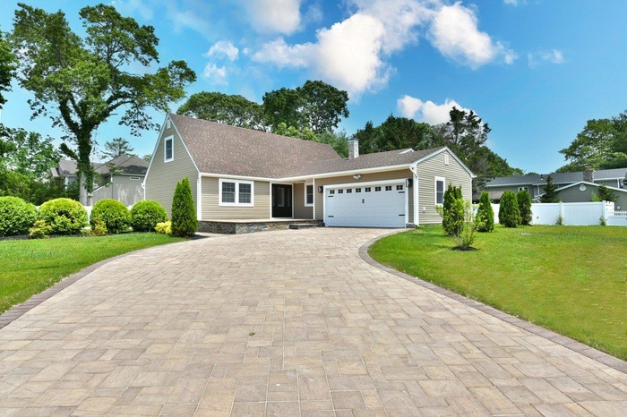 Ranch-style home with decorative driveway, an attached garage, a chimney, and a shingled roof