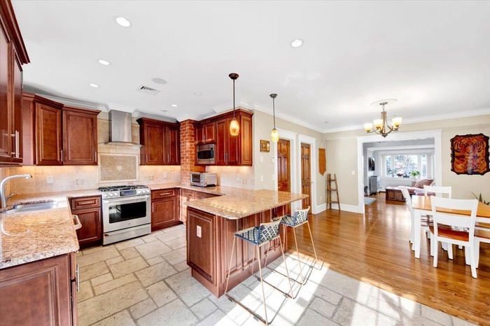 Kitchen featuring stainless steel appliances, a chandelier, tasteful backsplash, wall chimney exhaust hood, and a peninsula