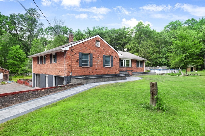 View of front of house featuring brick siding, an attached garage, a front lawn, and a chimney