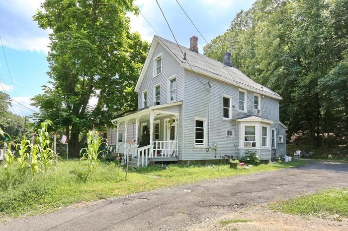 View of front of property featuring a porch, a chimney, and a shingled roof