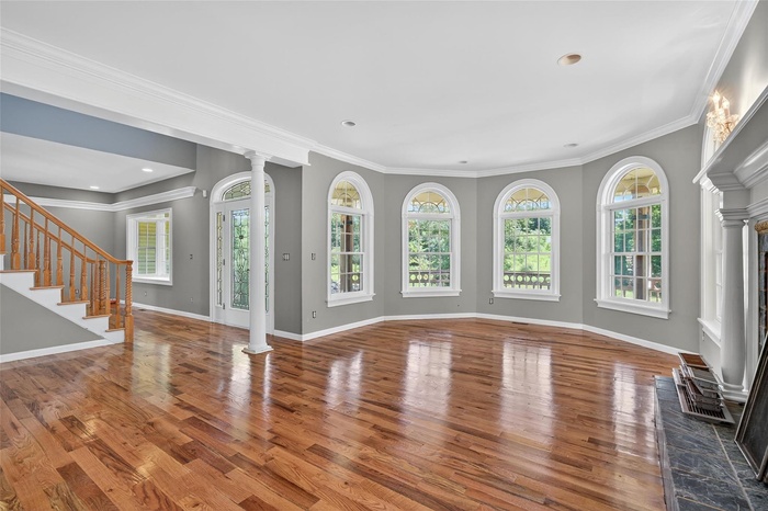 Unfurnished living room with hardwood / wood-style flooring, ornate columns, ornamental molding, a fireplace with raised hearth, and stairway