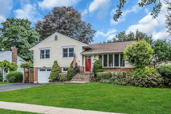 Split level home featuring brick siding, driveway, a garage, a front lawn, and a chimney