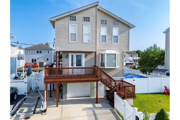 View of front of home with a garage, a wooden deck, concrete driveway, a fenced backyard, and a residential view