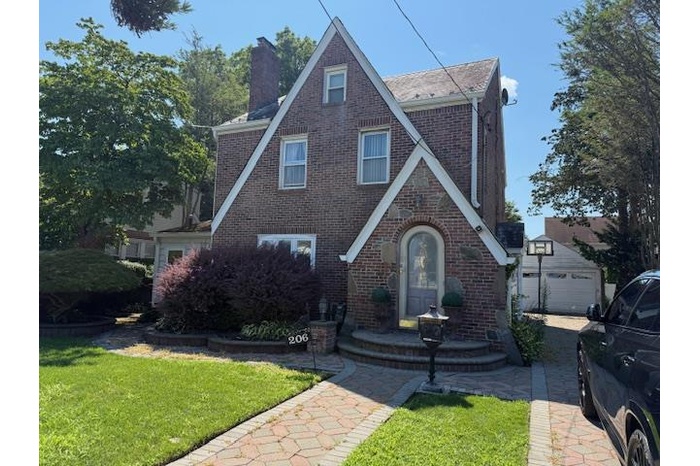 Tudor-style house with brick siding, a chimney, a front lawn, and a detached garage