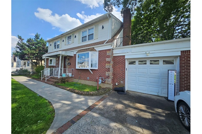 View of property with a chimney, a garage, brick siding, and asphalt driveway
