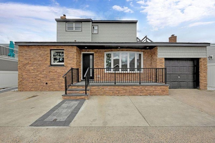 View of front of home with a garage, driveway, a chimney, a porch, and stone siding