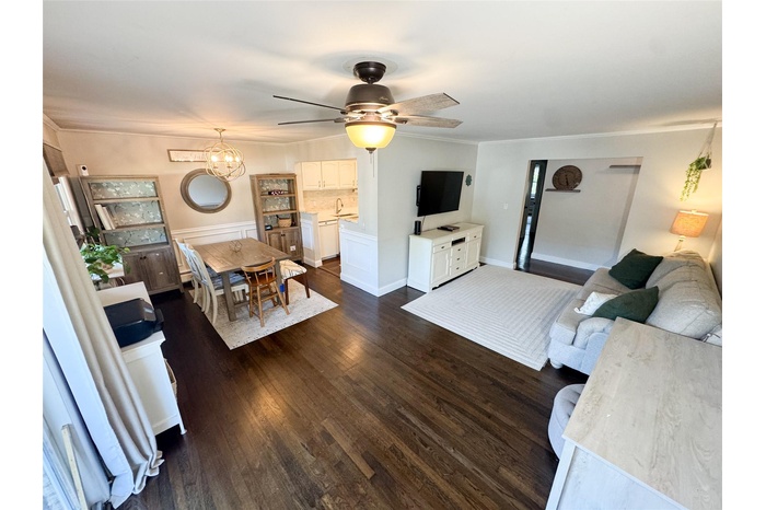 Living room with a ceiling fan, dark wood-type flooring, a chandelier, and crown molding