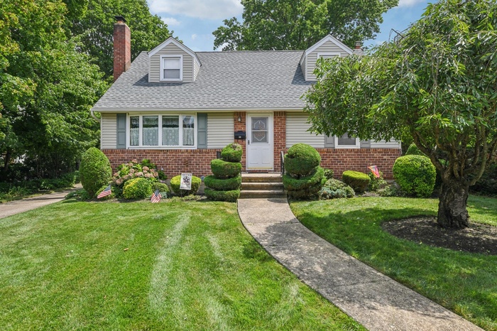 New england style home with a chimney, brick siding, a front yard, and a shingled roof