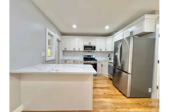 Kitchen featuring stainless steel appliances, light wood-style flooring, a peninsula, white cabinetry, and backsplash