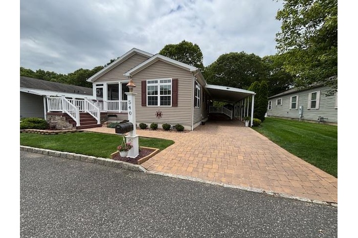 Manufactured / mobile home featuring a front yard, decorative driveway, and an attached carport
