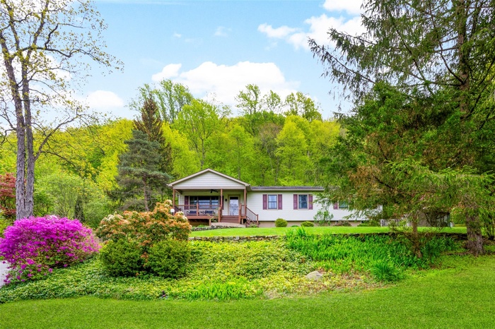 View of front facade with covered porch, a wooded view, and a carport