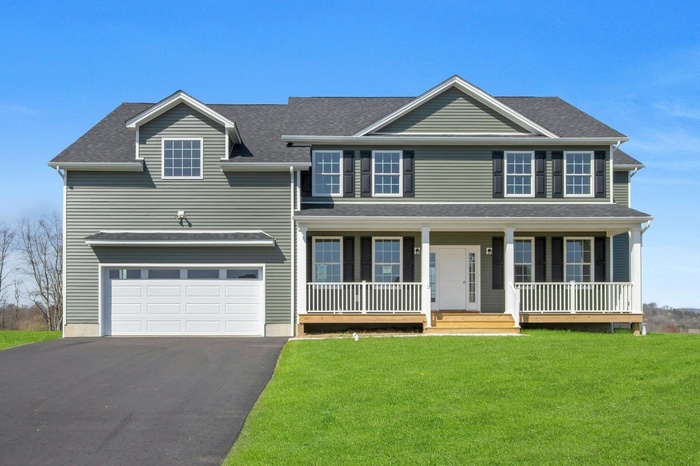 Colonial-style house featuring a porch, a shingled roof, a garage, driveway, and a front yard