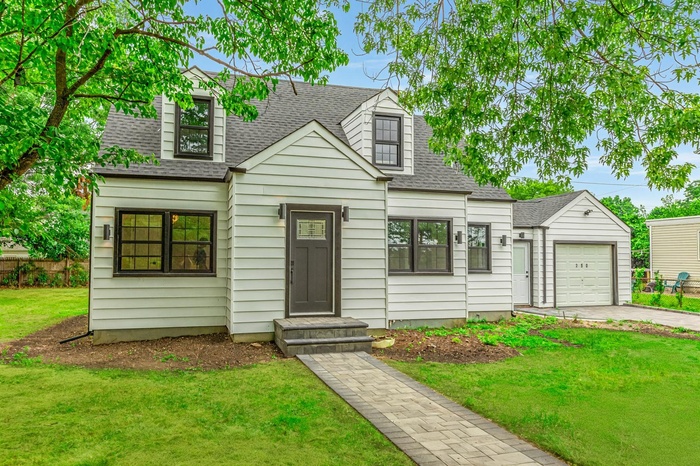 Cape cod home featuring roof with shingles, an attached garage, driveway, a front lawn, and entry steps