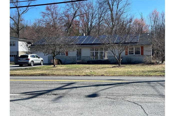 View of front of home with solar panels, a front yard, an attached garage, stone siding, and driveway