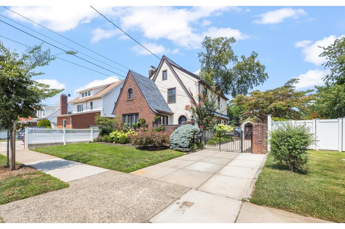 View of side of property with a gate, a fenced front yard, a chimney, brick siding, and a high end roof
