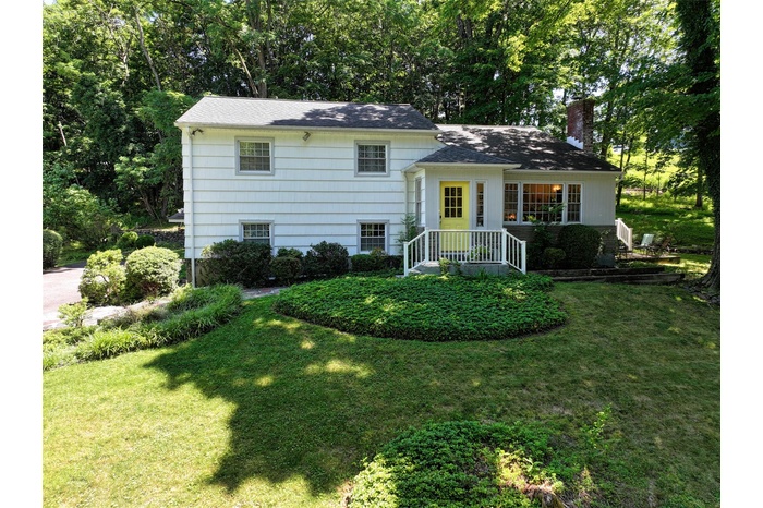 Tri-level home featuring a front yard, a chimney, and view of wooded area
