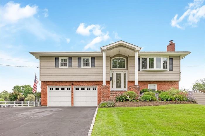 Raised ranch featuring asphalt driveway, brick siding, a garage, and a chimney