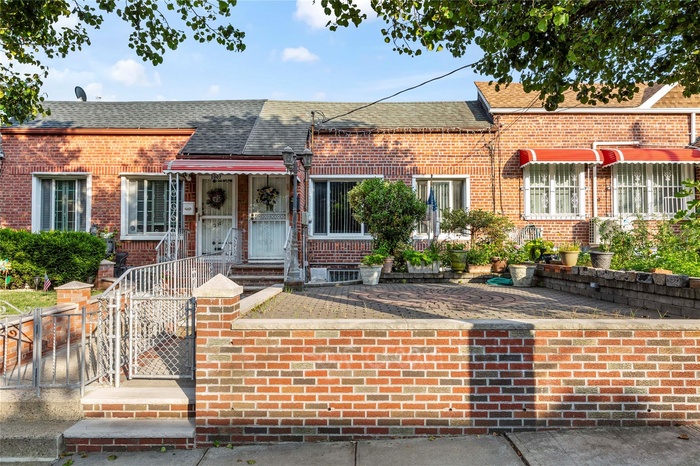 View of front facade with a shingled roof, a fenced front yard, brick siding, and a gate