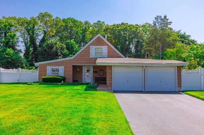 View of front of home with driveway, an attached garage, and view of wooded area