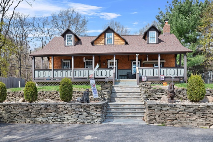 View of front facade featuring a chimney, a porch, and a shingled roof